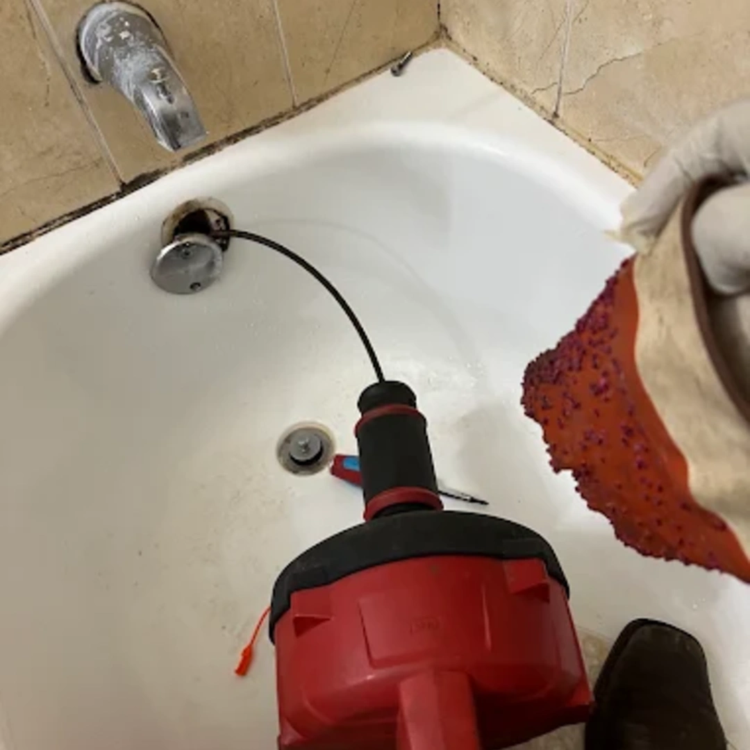 Professional plumber using a plumbing snake to unclog a bathtub drain in Miami FL