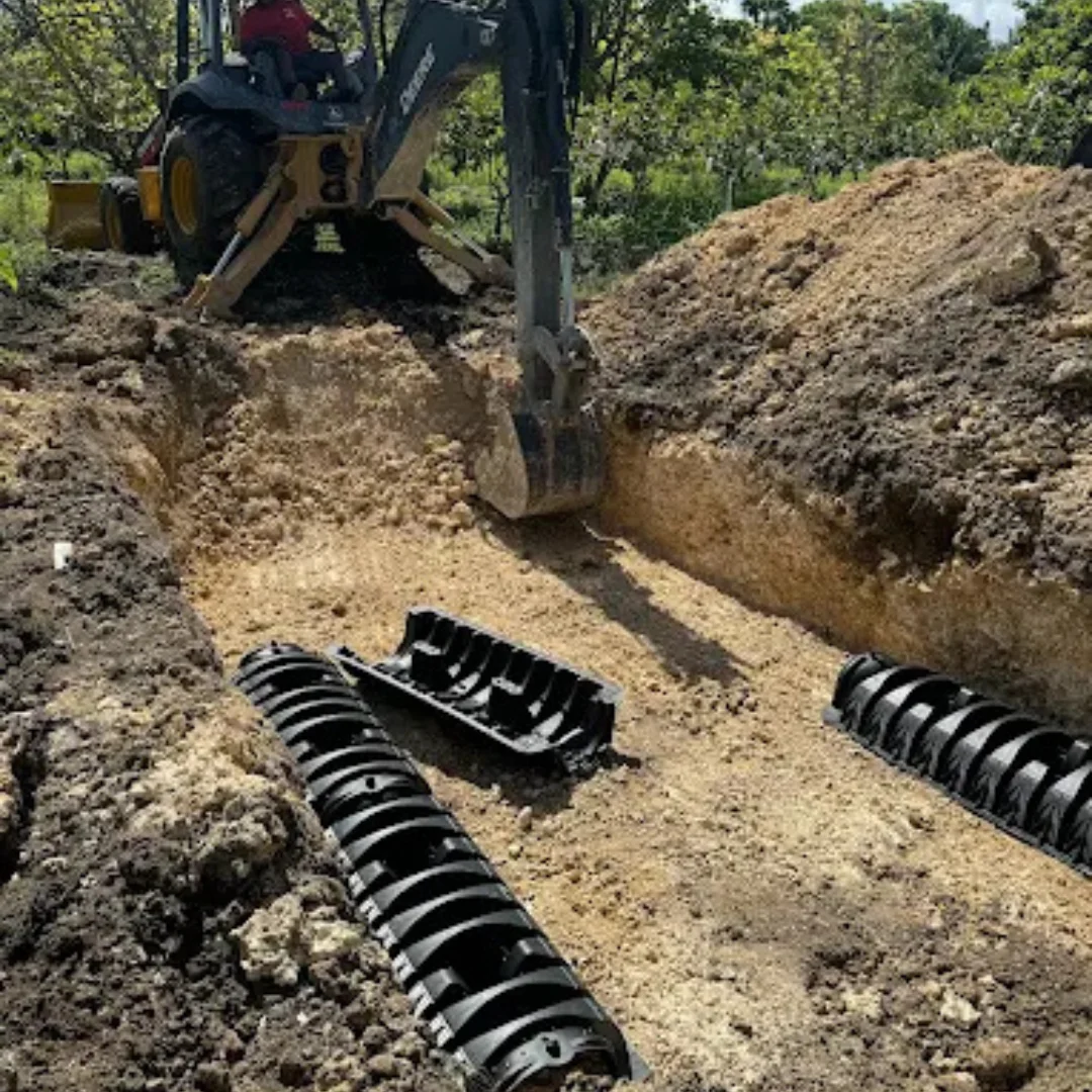 Excavator digging a trench for septic system drain field installation with plastic chamber pipes placed in the ground.